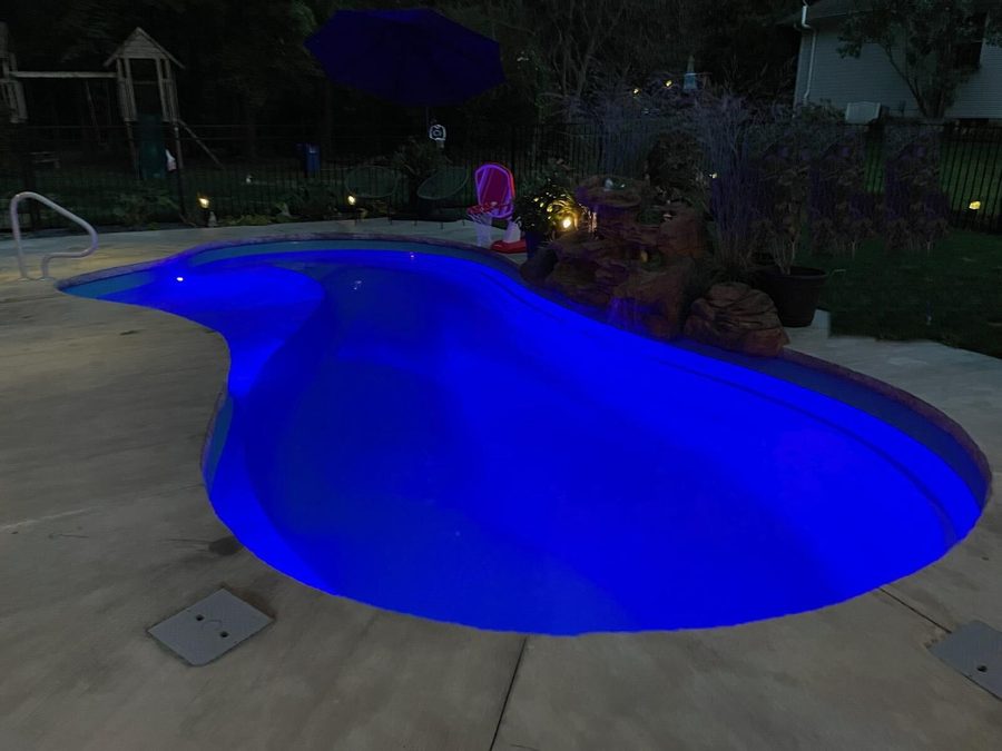 Freeform pool glowing blue at night beside a boulder waterfall